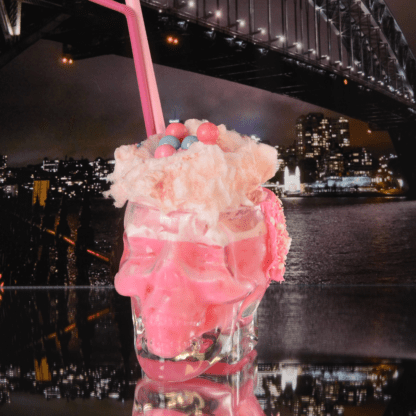 Cocktail rose avec bonbons et barbe à papa. Pailles roses dans verre en forme de crâne en verre transparent.